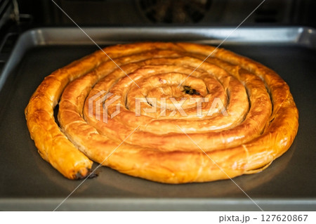 Golden Spiral Pastry Delight Freshly Baked Burek on a Baking Sheet in the Oven Golden Spiral Pastry Delight Freshly Baked Burek on a Baking Sheet in the Oven 127620867