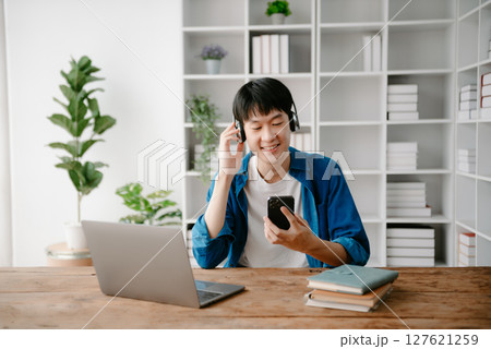 Smiling boy relaxing at home, she is playing music using smartphone tablet, laptop, and wearing white headphones. Smiling boy relaxing at home, she is playing music using smartphone tablet, laptop, and wearing white headphones. 127621259