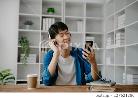 Smiling boy relaxing at home, she is playing music using smartphone tablet, laptop, and wearing white headphones. Smiling boy relaxing at home, she is playing music using smartphone tablet, laptop, and wearing white headphones. 127621280