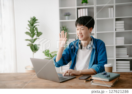 Male students note from the books at the Asian man library sitting at the desk using laptop computer and tablet to search an online informations. 127621286