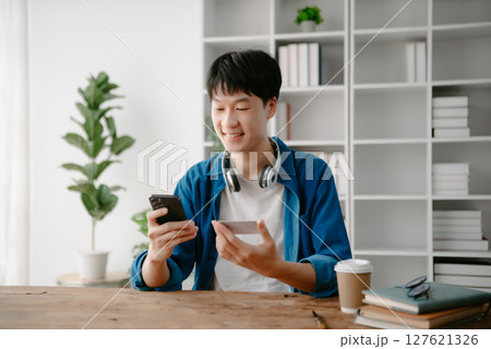 Man using smart phone for mobile payments online shopping,omni channel,sitting on table,virtual icons graphics interface screen in morning light 127621326