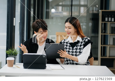 Two Asian businesswoman and man discuss investment project working and planning strategy with tablet laptop computer in office. Two Asian businesswoman and man discuss investment project working and planning strategy with tablet laptop computer in office. 127621569