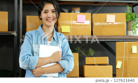 Asian woman startup small business at home office. Online seller entrepreneur young asian woman use tablet checking online order. Woman using tablet check stock goods supply delivery package shipping 127621640