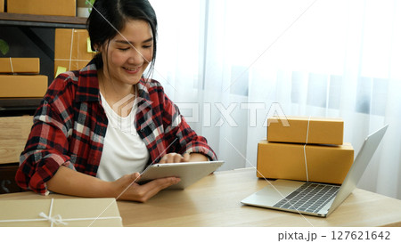 Asian woman startup small business at home office. Online seller entrepreneur young asian woman use tablet checking online order. Woman using tablet check stock goods supply delivery package shipping Asian woman startup small business at home office. Online seller entrepreneur young asian woman use tablet checking online order. Woman using tablet check stock goods supply delivery package shipping 127621642
