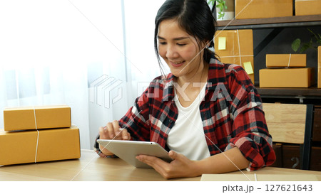 Asian woman startup small business at home office. Online seller entrepreneur young asian woman use tablet checking online order. Woman using tablet check stock goods supply delivery package shipping 127621643