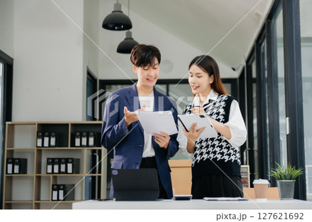 Asian business colleague business presents and explains and using laptop and tablet. Teamwork, financial marketing team,   while sitting in modern office room. 127621692