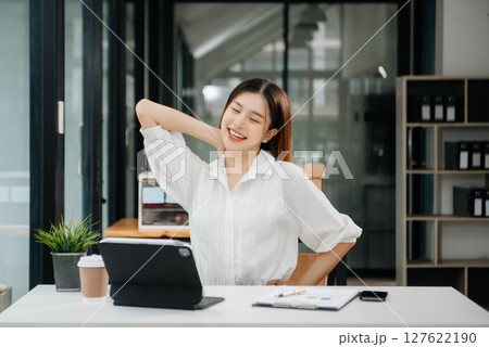 Overworked young Asian businesswoman office worker suffering from neck pain after had a long day at her office desk. office syndrome concept Overworked young Asian businesswoman office worker suffering from neck pain after had a long day at her office desk. office syndrome concept 127622190