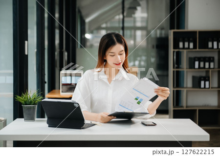 Young beautiful woman typing on tablet and laptop while sitting at the working white table modern office 127622215