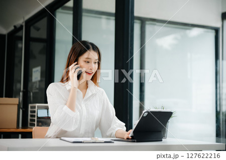 Young beautiful woman typing on tablet and laptop while sitting at the working white table modern office Young beautiful woman typing on tablet and laptop while sitting at the working white table modern office 127622216