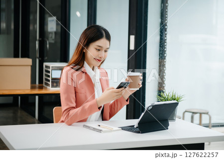 Young beautiful woman typing on tablet and laptop while sitting at the working white table modern office Young beautiful woman typing on tablet and laptop while sitting at the working white table modern office 127622257