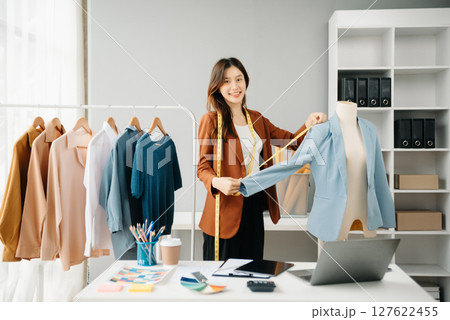 Fashion blogger concept, Young Asian women selling clothes on video streaming.Startup small business SME, using smartphone or tablet taking receive 127622455