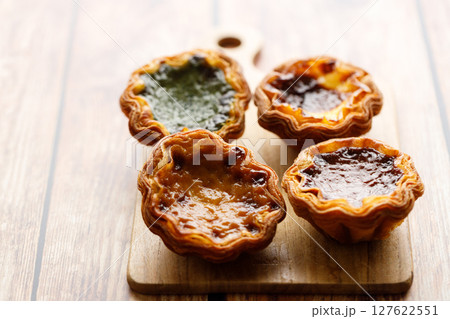Stack of assorted Portuguese sweet dessert egg tart or Pastel de Nata on wooden board on wooden table. Stack of assorted Portuguese sweet dessert egg tart or Pastel de Nata on wooden board on wooden table. 127622551