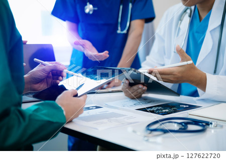 Medical team having a meeting with doctors in white lab coats and surgical scrubs seated at a table discussing a patients working online using computers Medical team having a meeting with doctors in white lab coats and surgical scrubs seated at a table discussing a patients working online using computers 127622720