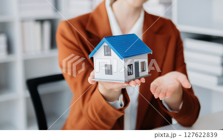 Young real estate agent worker working with laptop and tablet at table in office and small house beside it. Young real estate agent worker working with laptop and tablet at table in office and small house beside it. 127622839