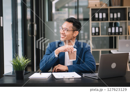 Young handsome man typing on tablet and laptop while sitting at the working wooden table modern office 127623129