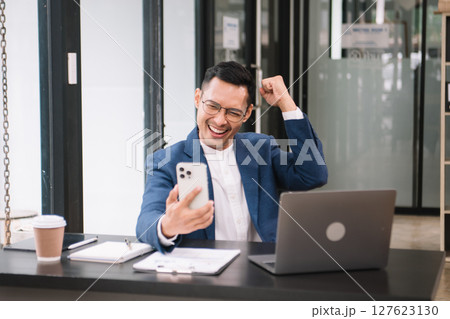 Young handsome man typing on tablet and laptop while sitting at the working wooden table modern office Young handsome man typing on tablet and laptop while sitting at the working wooden table modern office 127623130