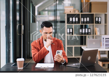 Young handsome man typing on tablet and laptop while sitting at the working wooden table modern office 127623135
