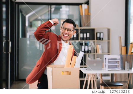 Happy and excited young beautiful Asian man office worker celebrating her resignation, carrying her personal stuff. leaving job, changing or company. 127623238