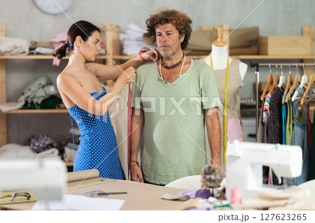 Young male tailor measuring female client in sewing workshop 127623265