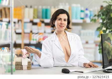 Female pharmacist in unbuttoned gown invites to pharmacy 127623415