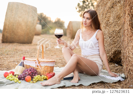 Portrait of woman in top and shorts with glass of red wine on picnic 127623631