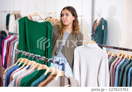 Portrait woman choosing new clothes on hangers in shop 127623761