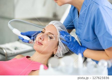 Young visitor receiving hardware electric massage and absorb blackheads and deeply clear skin by doctor in beauty clinic. Hardware cosmetology. Beautician hands in gloves makes face skin treatment for 127623836