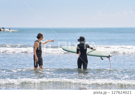 海でサーフィンを教える年配男性と若い女性の後ろ姿 127624021