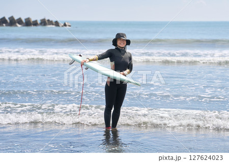 ボードを持って海に立つ女性サーファー ボードを持って海に立つ女性サーファー 127624023
