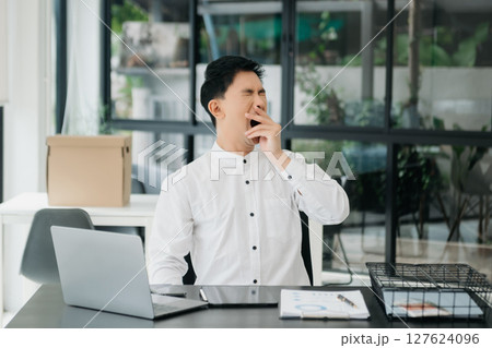 Frustrated young businessman working on a laptop computer sitting at his working place 127624096