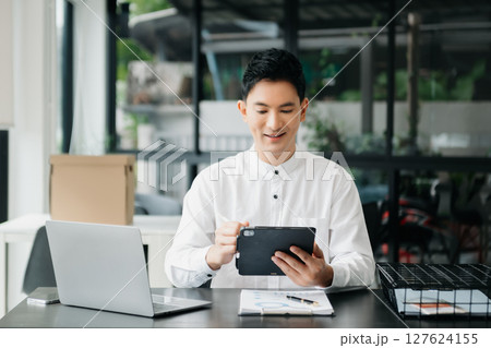 Young handsome man typing on tablet and laptop while sitting at the working wooden table office Young handsome man typing on tablet and laptop while sitting at the working wooden table office 127624155