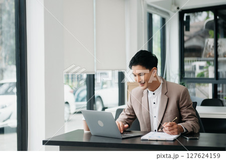 Young handsome man typing on tablet and laptop while sitting at the working wooden table office 127624159