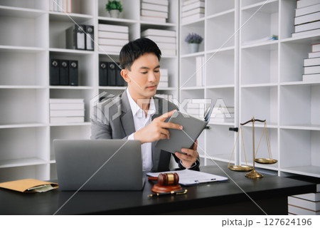 Asian man lawyer reading legal book with gavel on table in office. justice and law ,attorney concept. Asian man lawyer reading legal book with gavel on table in office. justice and law ,attorney concept. 127624196
