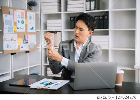 Overworked young Asian businessman office worker suffering from neck pain after had a long day at desk. office syndrome concept Overworked young Asian businessman office worker suffering from neck pain after had a long day at desk. office syndrome concept 127624270