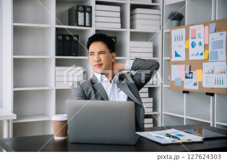 Overworked young Asian businessman office worker suffering from neck pain after had a long day at desk. office syndrome concept 127624303
