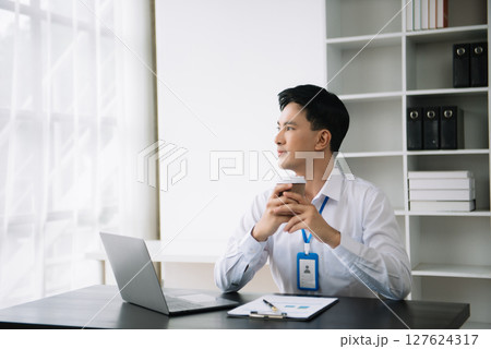 Young Asian business man using laptop and tablet while sitting at her working place. Concentrated at work. Young Asian business man using laptop and tablet while sitting at her working place. Concentrated at work. 127624317
