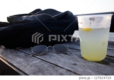 海辺の木製のテーブルに置かれたサングラスと黒いリックと黒い帽子と柑橘のソーダ 海辺の木製のテーブルに置かれたサングラスと黒いリックと黒い帽子と柑橘のソーダ 127624729