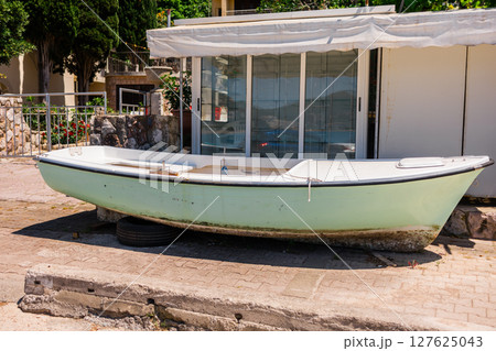 Old boat on asphalt near shop. Coastal lifestyle, fishing culture, and marine equipment storage 127625043