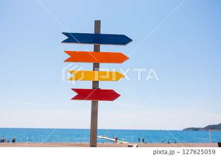 Wooden beach signpost with arrows on seaside promenade, copy space. Summer vacation, coastal leisure, and travel direction concept. 127625059
