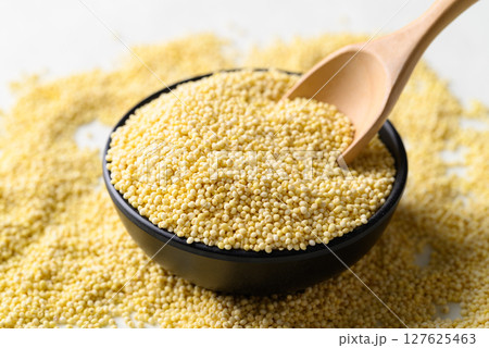 Yellow millet grain in black bowl with spoon, Food ingredient 127625463