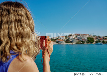 Woman taking photo with instant camera near sea on summer vacation Woman taking photo with instant camera near sea on summer vacation 127625866