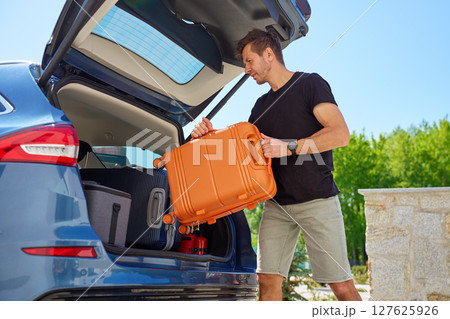 Man placing suitcase into car trunk before summer trip Man placing suitcase into car trunk before summer trip 127625926