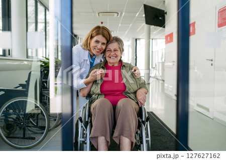 Elderly patient in wheelchair and female physician smiling at clinic. 127627162