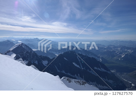 Tranquil Lake With Lush Green Forest, Snow-Capped Mountain, Blue Sky And White Clouds Tranquil Lake With Lush Green Forest, Snow-Capped Mountain, Blue Sky And White Clouds 127627570