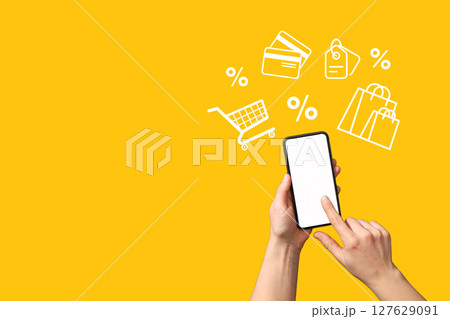 A user shops online on a smartphone against a bright yellow background A user shops online on a smartphone against a bright yellow background 127629091