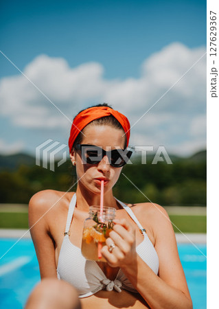 Young woman sitting by swimming pool and drinking limonade. Young woman sitting by swimming pool and drinking limonade. 127629367