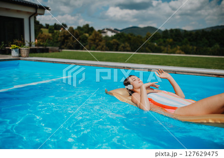 Top view of young woman in swimming pool outdoors on floating bed, relaxing. 127629475