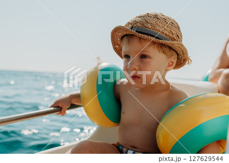 A small boy with arm floaties sitting on boat on summer holiday. A small boy with arm floaties sitting on boat on summer holiday. 127629544