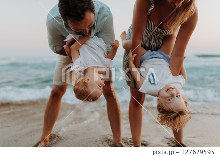 A young family with two toddler children having fun on beach on summer holiday. 127629595
