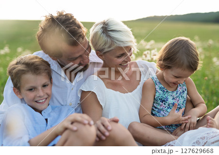 Young family with small children in summer nature at sunset, sitting in the grass. 127629668